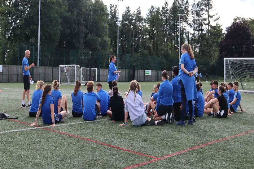 The uSports coaching team sitting on the pitch during a training day briefing
