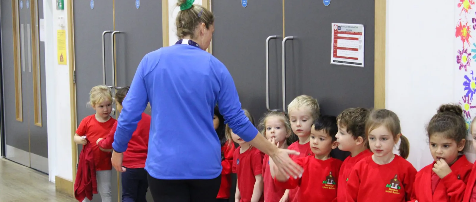 A uSports coach greeting a line of infant school children before a session