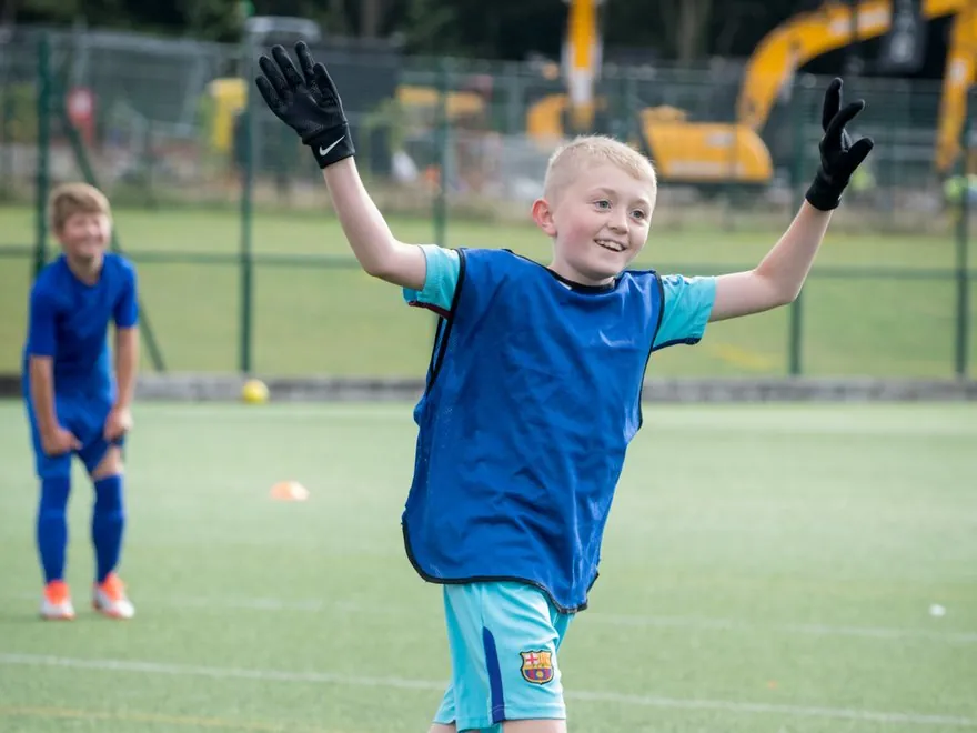 A child celebrating with both arms raised at a uSports football class