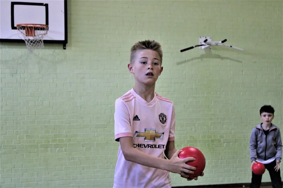 A child holding a red dodgeball in a sports hall