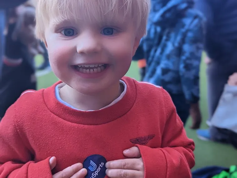 A smiling toddler holding a uSports badge