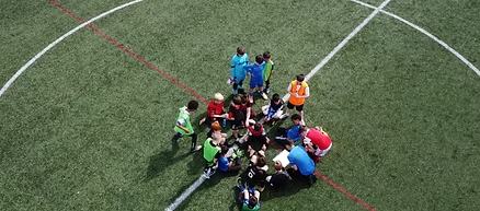 Children gathered round a coach on a football pitch, seen from above