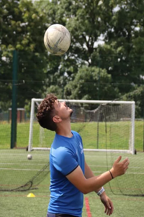 A uSports coach heading a football on the pitch