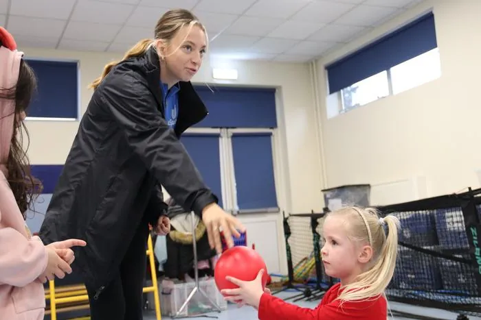 A uSports coach handing a ball to a child during an indoor session
