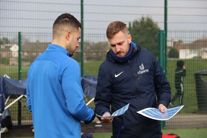 Two uSports coaches reviewing session stickers pitchside