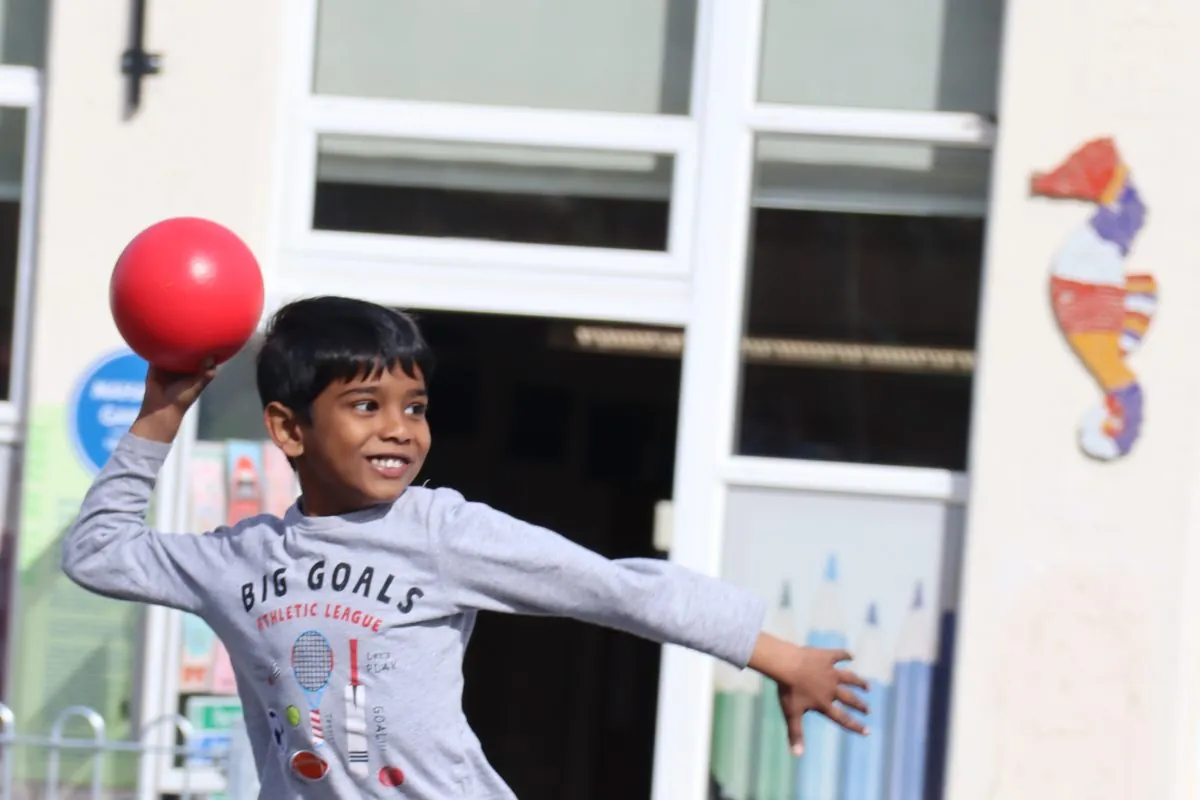 A child throwing a red dodgeball in a school playground