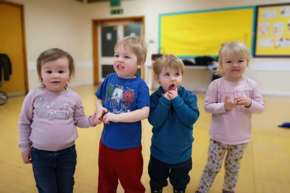 Four toddlers standing together during a session in a hall