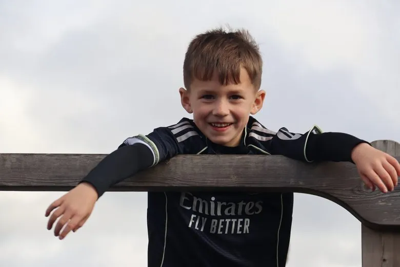 Smiling boy in a football shirt leaning over a wooden fence