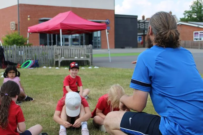 A uSports coach sitting with a group of children on the school field