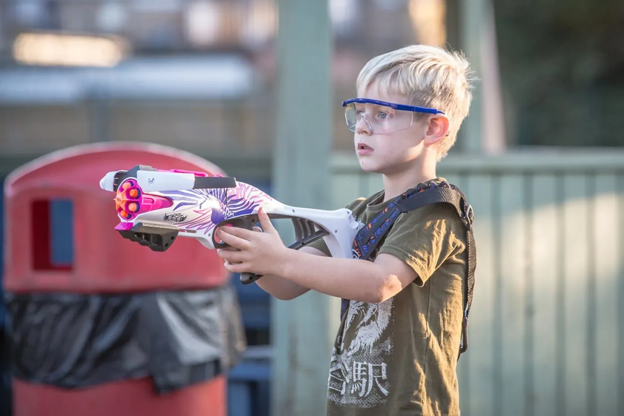 A child aiming a NERF blaster with safety glasses on