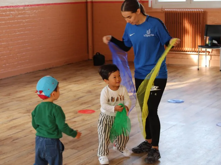 A uSports coach running a scarves activity with two toddlers